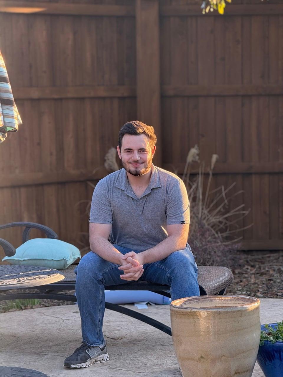 Christopher seated by a fence